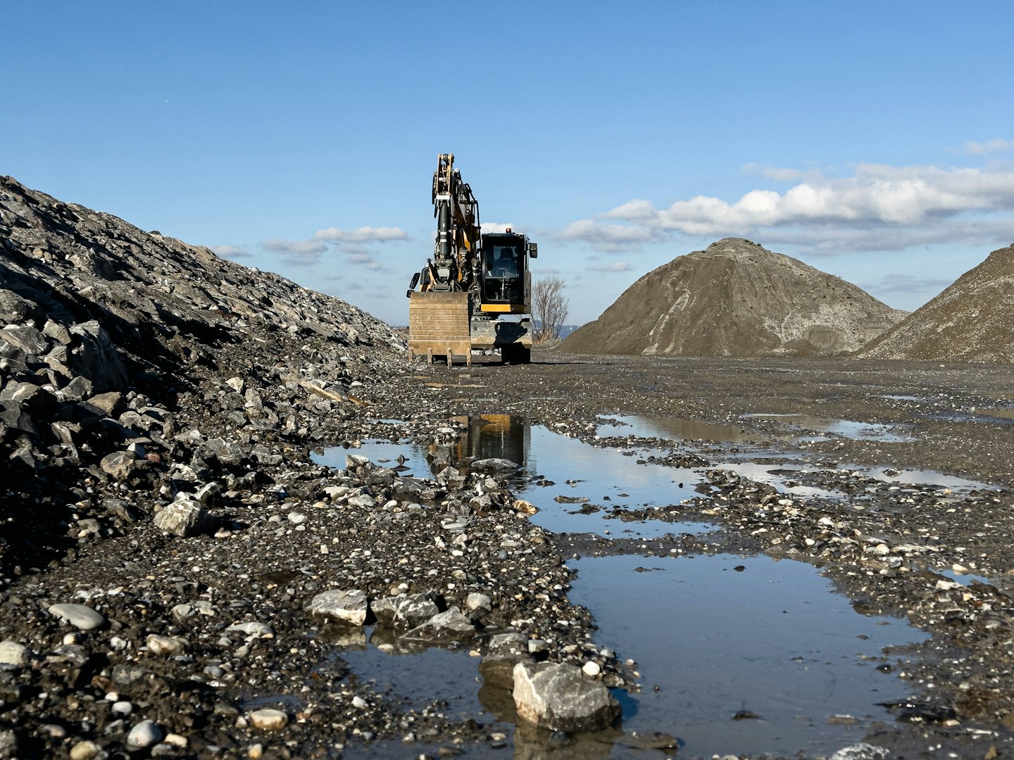 Yellow and grey excavator parked in a gravel quarry.