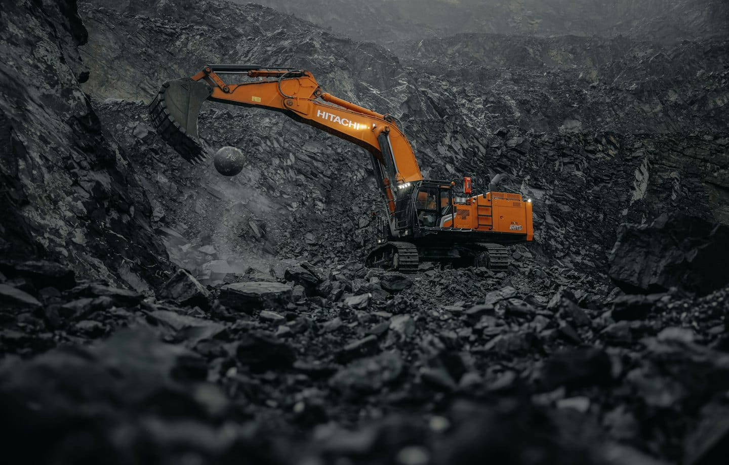 Orange excavator in rock quarry dislodging large boulder.