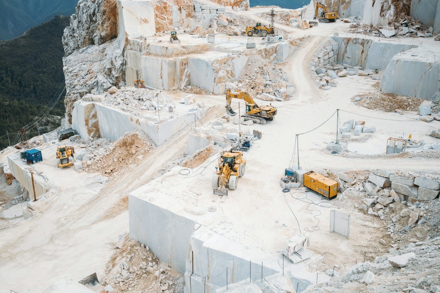 Heavy machinery operating in an expansive white marble quarry.