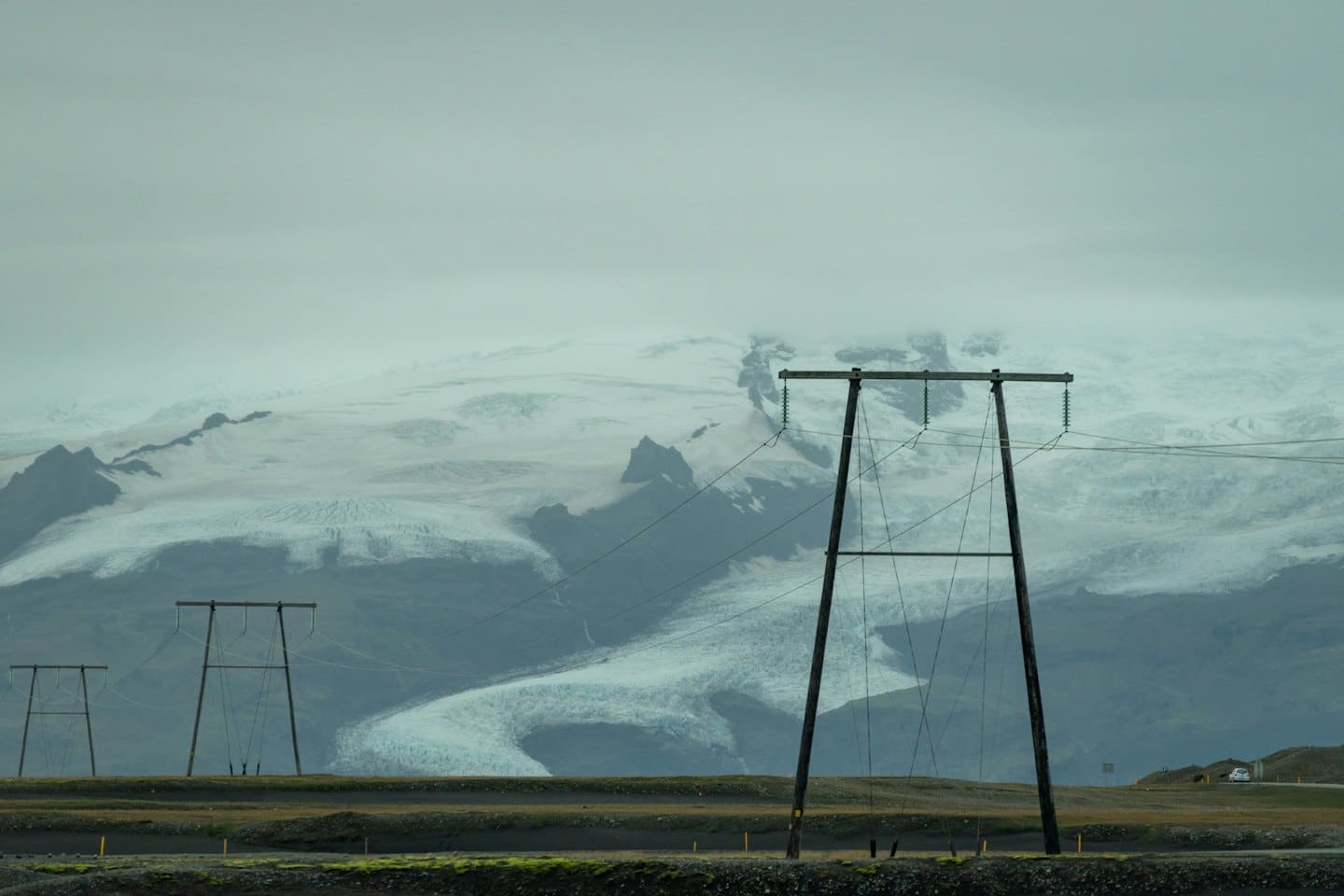 Power lines stand before a snow-covered mountain range with a glacier.