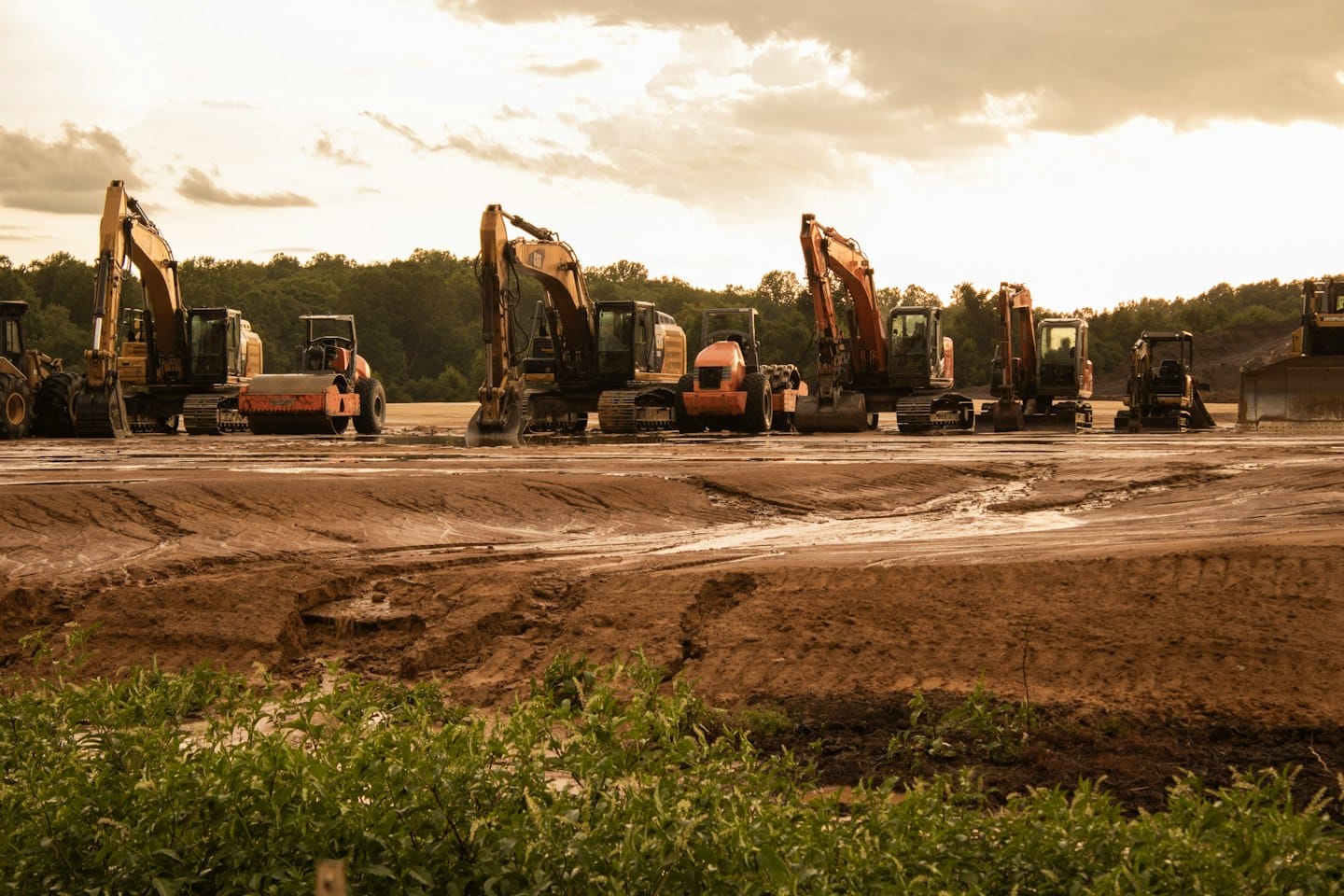 Construction machinery parked on a muddy graded earth site.