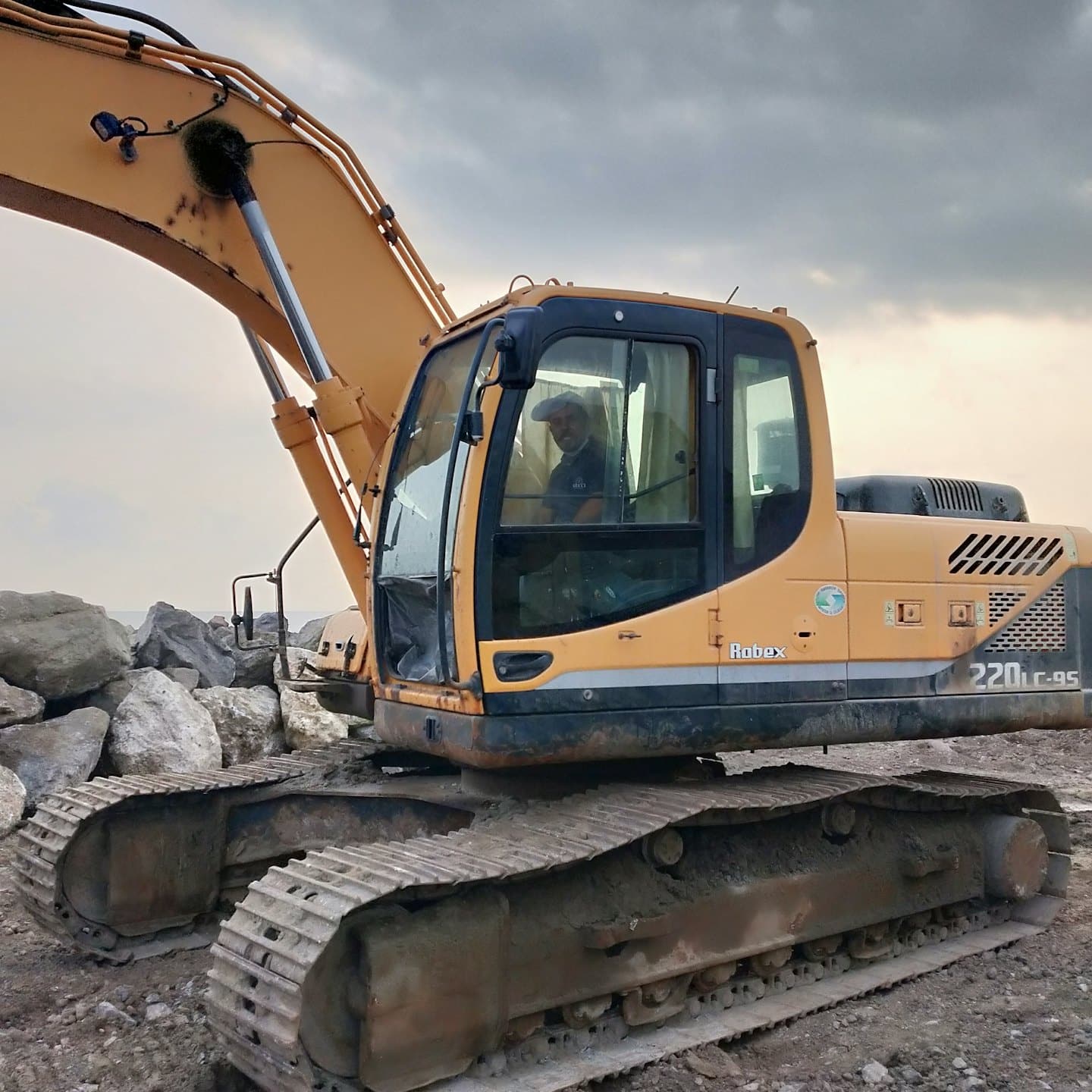 Construction worker operates yellow excavator on rocky shoreline.