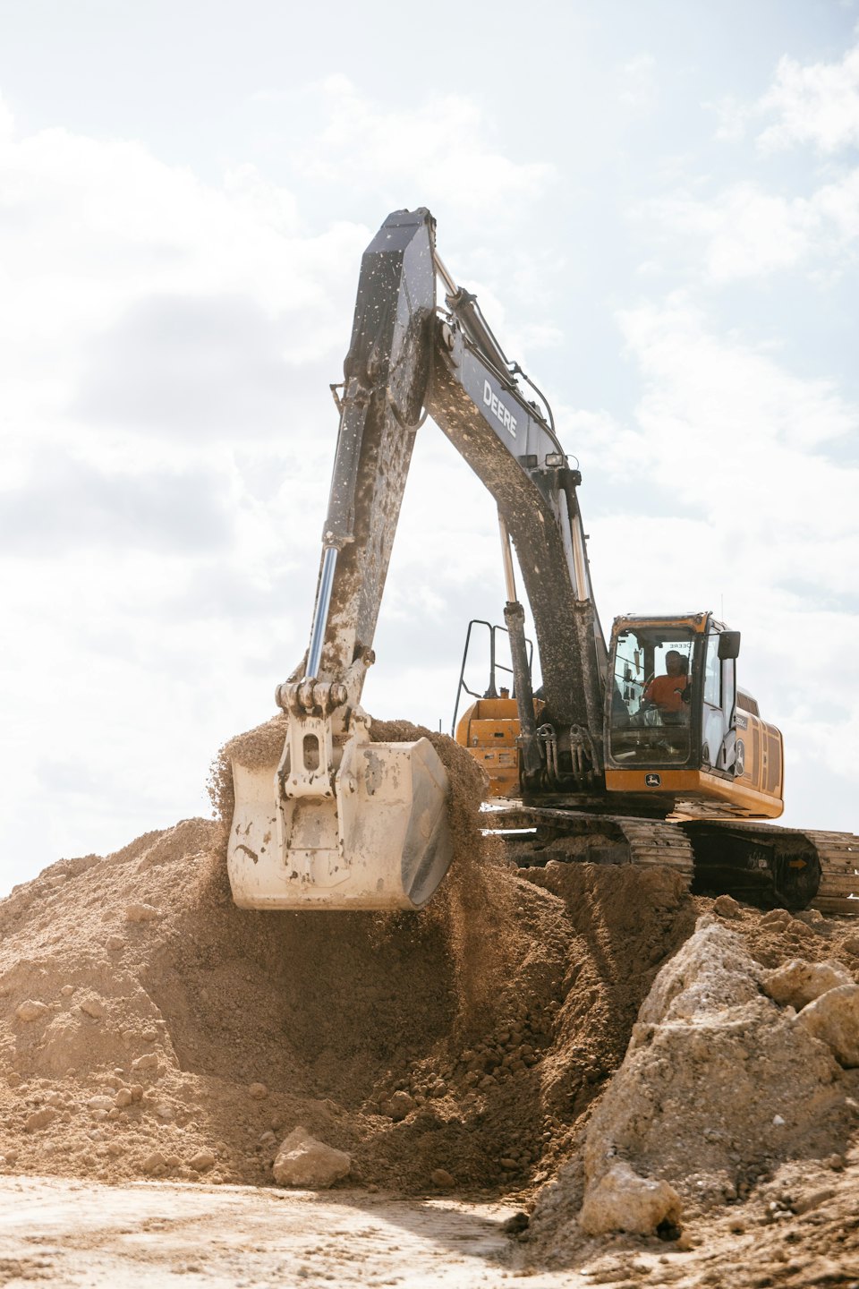 Operator driving a yellow John Deere excavator scooping soil.